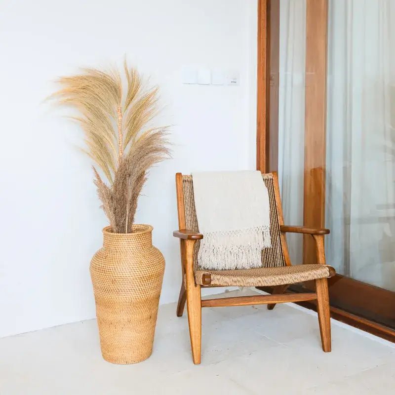 Rattan-Bodenvase Kidung mit Pampasgras neben einem Holzstuhl im modernen Natur-Look.