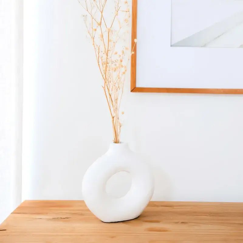 Weiße Tonvase Nusa in moderner Ringform auf Holztisch im hellen Wohnambiente.