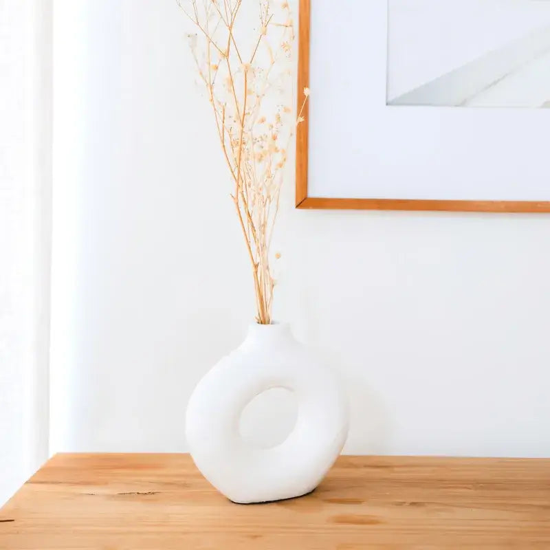 Weiße Tonvase Nusa in moderner Ringform auf Holztisch im hellen Wohnambiente.