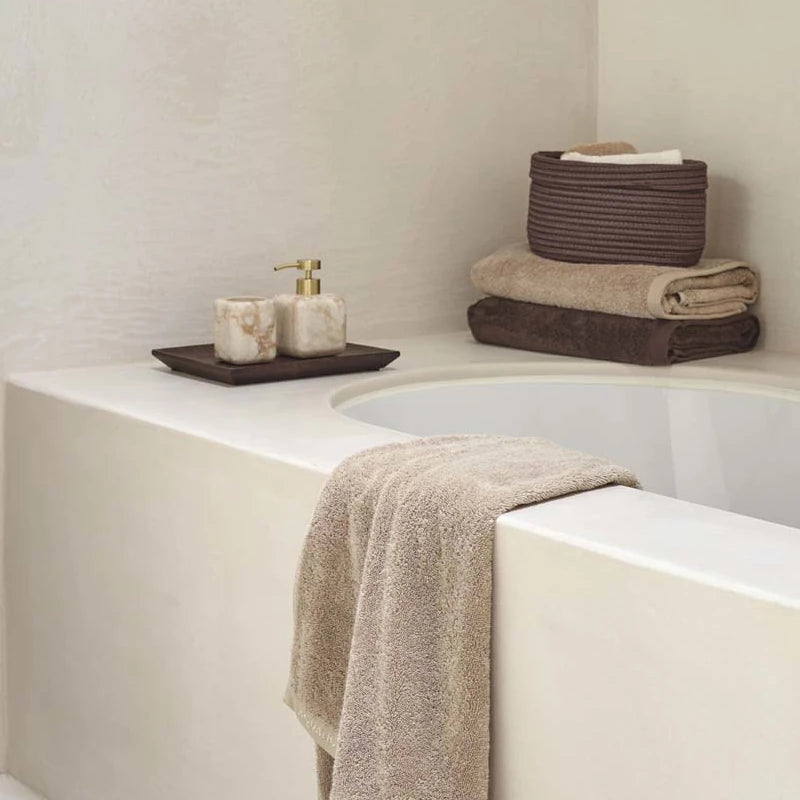 Badezimmer-Regal mit gefalteten Handtüchern in Erdtönen, Rattan-Korb und Badaccessoires in Truffle und Creme
