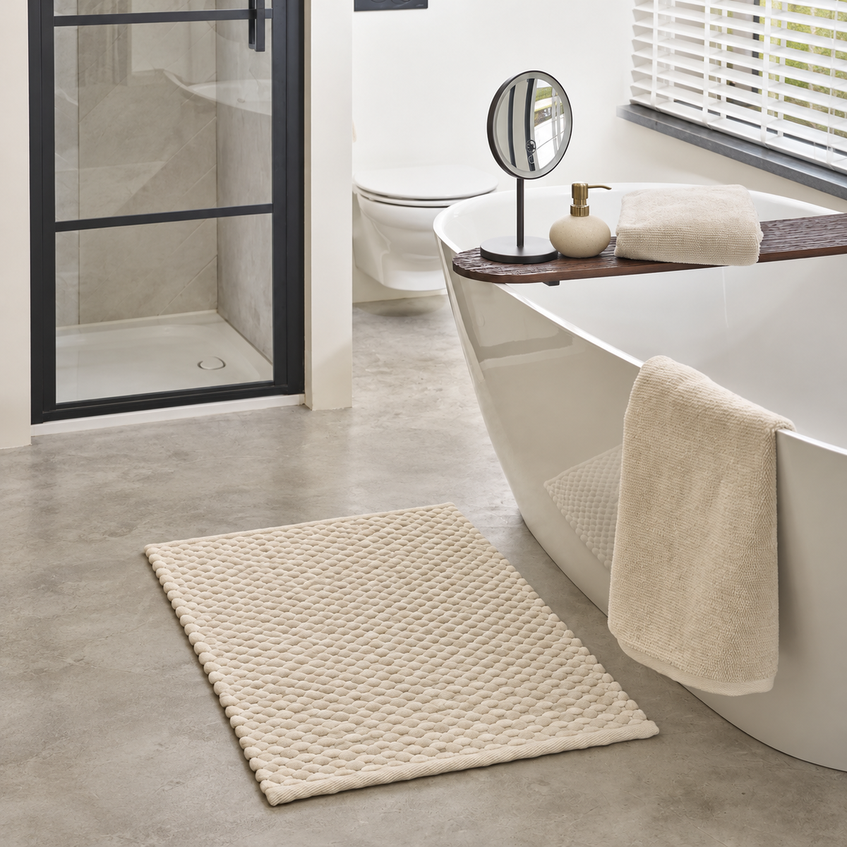 Helles Badezimmer mit cremefarbenem Badteppich, freistehender Badewanne und abgestimmten Badaccessoires
