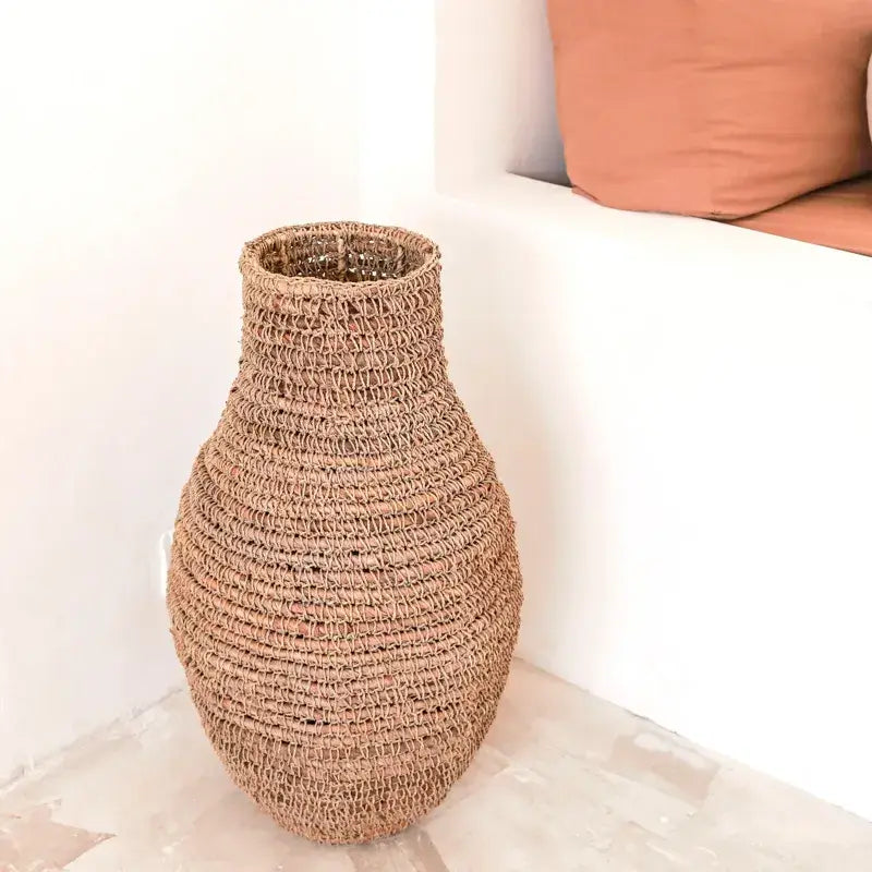 Große geflochtene Bodenvase Sakra aus Naturfasern in hellem Wohnambiente neben Sitzbank.