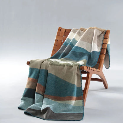 Kuscheldecke Iceland Horizon über einem Sessel drapiert, Wellenmuster in Blau, Beige und Grün