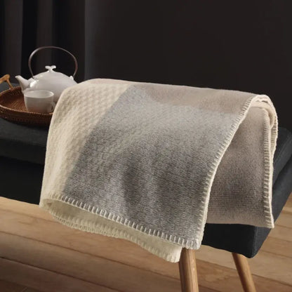 Merinowolle Kuscheldecke in Naturtönen auf einer Bank im Wohnzimmer, weich und strukturiert gewebt