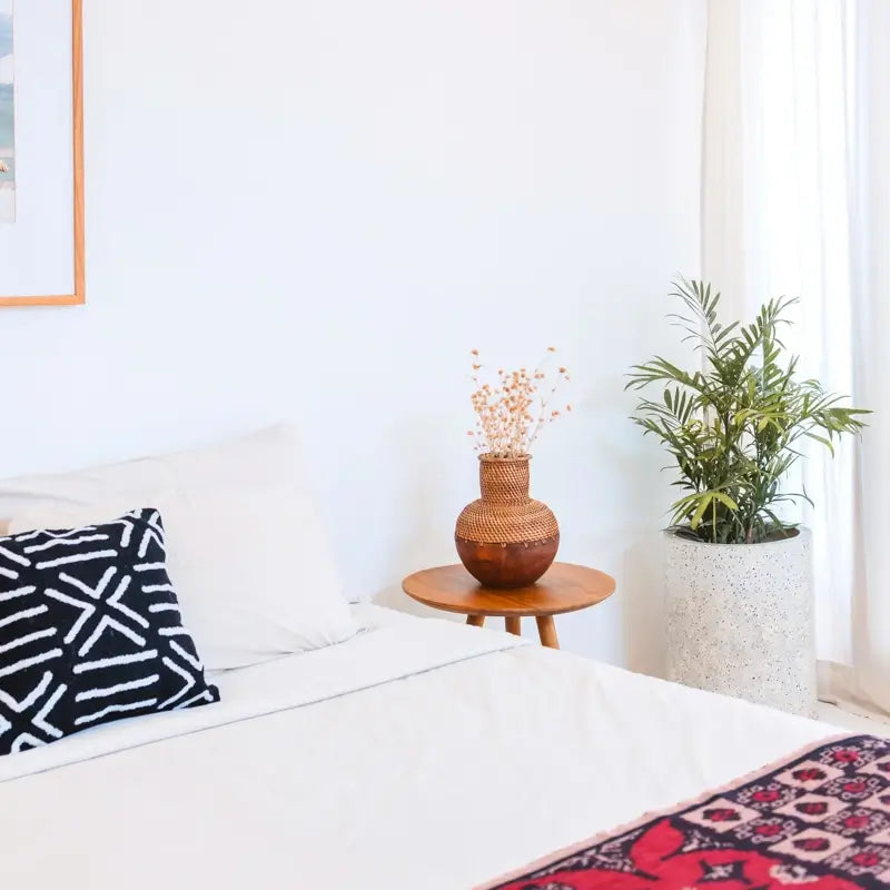 Rattan Vase Kamari als Wohnaccessoire auf rundem Holztisch neben Bett und Pflanze